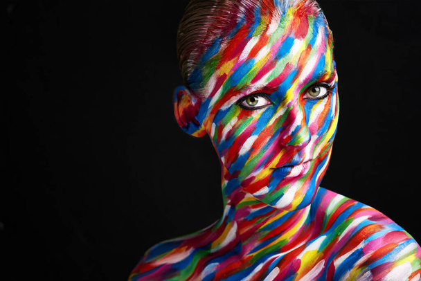 Το μακιγιάζ είναι τέχνη. Στιγμιότυπο μιας νεαρής γυναίκας που ποζάρει με έντονα χρωματιστά χρώματα στο πρόσωπό της πάνω σε μαύρο φόντο. - Φωτογραφία, εικόνα