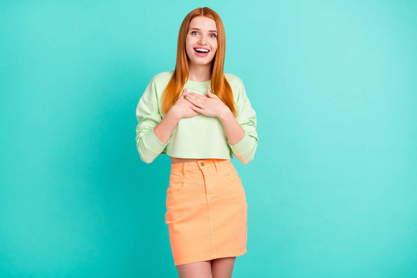Photo portrait of red haired girl smiling amazed thankful keeping hands on chest isolated vibrant teal color background - Фото, зображення
