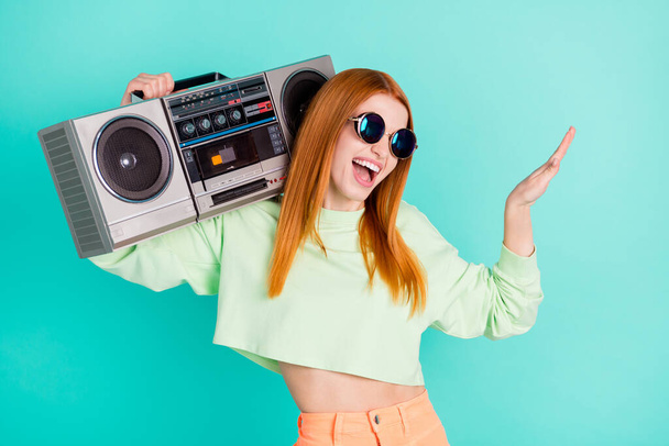 Photo portrait of red haired girl smiling keeping boom box enjoying music isolated vibrant teal color background - Фото, изображение