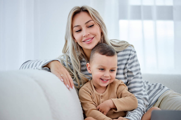 smiling young mother with little kid sit on sofa in living room have fun using laptop - Foto, Bild