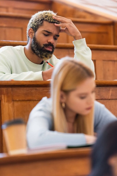 アフリカ系アメリカ人の学生は、大学の講堂でぼやけた友人の近くに座って  - 写真・画像