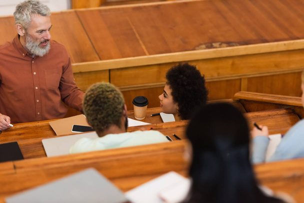 Mosolygó tanár kezében kréta közelében afro-amerikai diákok az egyetemen  - Fotó, kép