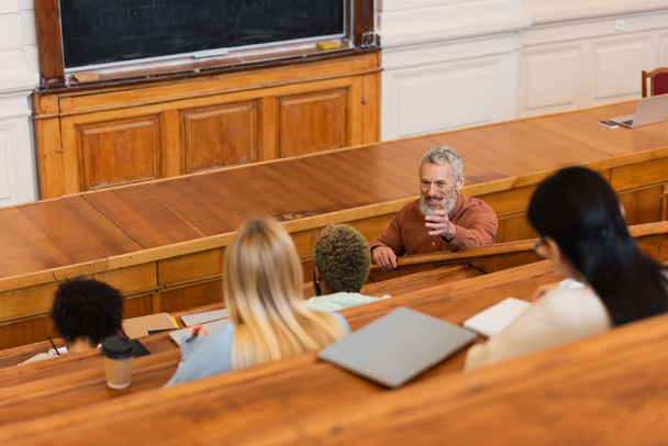 Positive teacher talking to interracial students in auditory of university  - Zdjęcie, obraz