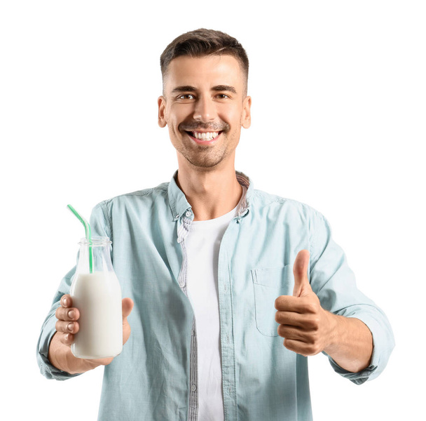 白い背景に親指アップを示すミルクのボトルを持つ若い男 - 写真・画像