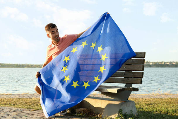 Молодий чоловік з прапором Європейського Союзу біля річки на вулиці. - Фото, зображення