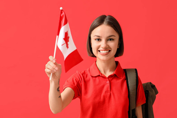 Beautiful young woman with Canadian flag and backpack on color background - Photo, Image