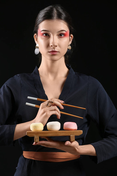 Beautiful young woman with tasty Japanese mochi on black background - Foto, afbeelding