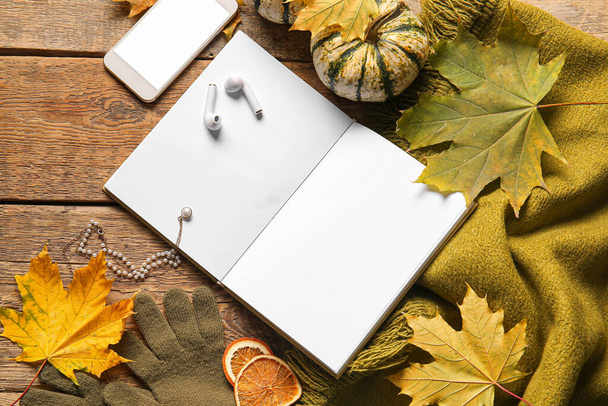 Blank book, mobile phone, earphones and autumn decor on wooden background - Foto, afbeelding