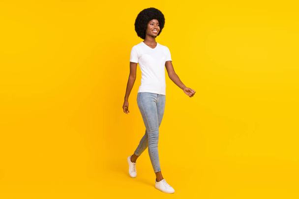 Full length photo of funny charming dark skin lady wear white t-shirt walking looking empty space smiling isolated yellow color background - Photo, Image