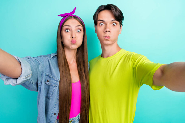 遊び心のあるコメディの若者のカップルの写真セルフィーはターコイズ色の背景に隔離されたピンクの黄色のTシャツのヘアバンドを身に着けています - 写真・画像