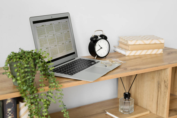 Laptop with digital calendar and eyeglasses on shelf near light wall - Photo, Image