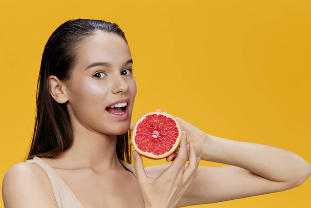 mooie vrouw eten grapefruit in handen glimlach vitaminen dieet gele achtergrond - Foto, afbeelding