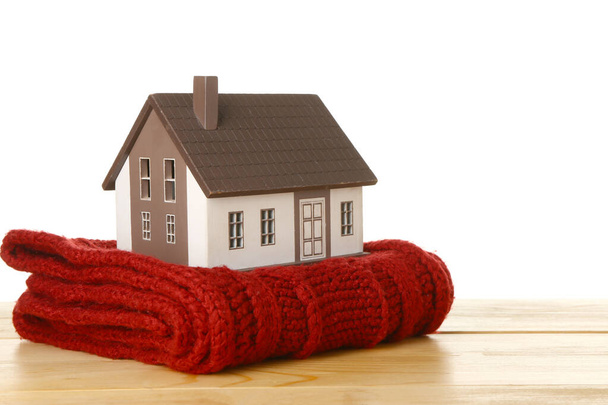 Modelo de casa con bufanda roja sobre mesa sobre fondo blanco. Concepto de calefacción - Foto, imagen