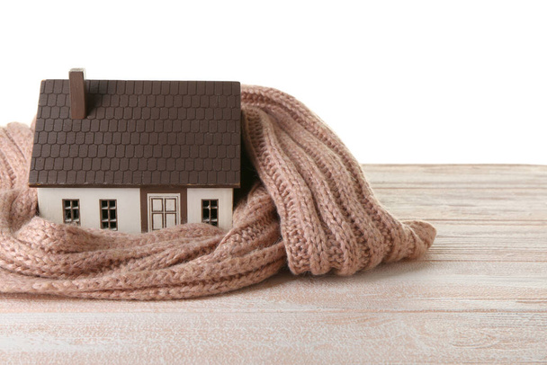 House model with knitted scarf on table against white background. Heating concept - Photo, Image
