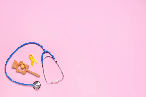 Zlatá stuha vědomí, chrastítko a stetoskop na barevném pozadí. Mezinárodní den rakoviny v dětství - Fotografie, Obrázek