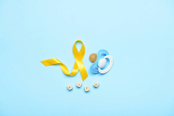 Arany tudatosság szalag, cumi és szó HOPE kék háttérrel. A gyermekkori rák nemzetközi napja - Fotó, kép