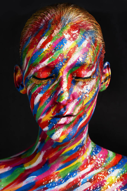 La beauté embrasse chaque couleur. Plan studio d'une jeune femme posant avec de la peinture aux couleurs vives sur son visage sur un fond noir. - Photo, image