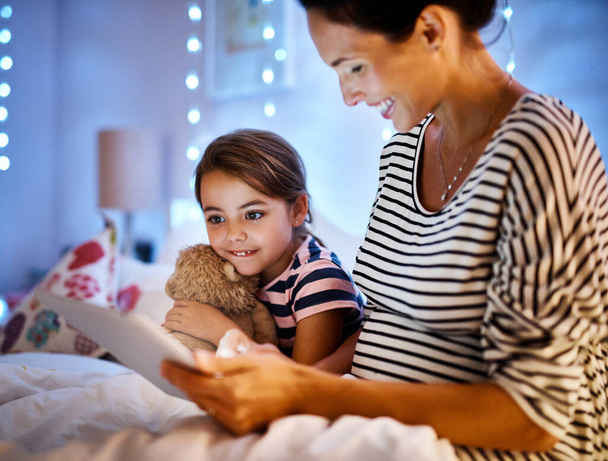 Engrossed in an interactive story. Cropped shot of an attractive young pregnant woman reading her daughter a bedtime story on a tablet. - Foto, Bild