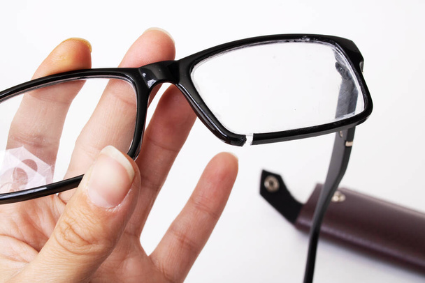 gebroken bril in de hand op een grijze achtergrond close-up - Foto, afbeelding