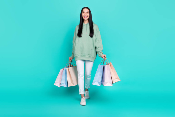 Full size photo of nice millennial brunette lady go with bags wear hoodie trousers sneakers isolated on teal background - Fotoğraf, Görsel