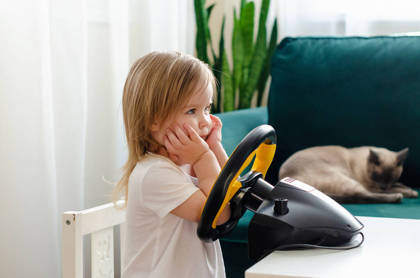 小さな女の子は、コンピュータのステアリングホイールで遊んでいる。女の子はビデオゲームをプレイ-カーレース。将来のドライバー。プロの運転の準備を。車を運転する子供 - 写真・画像