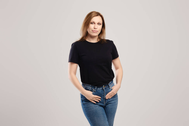 Young woman in black t shirt and jeans posing over grey background - Photo, image