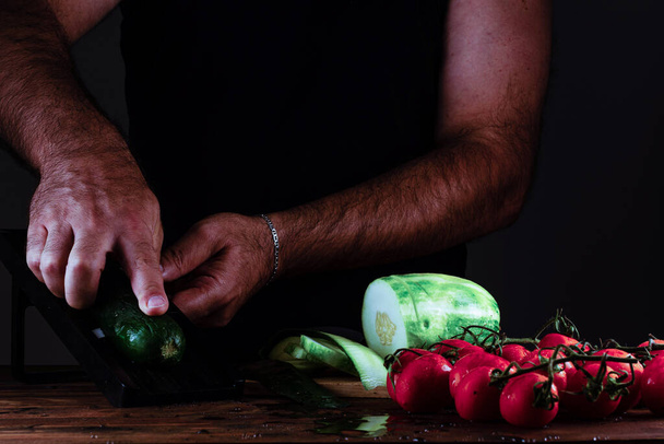 Человек держит кусок свежих овощей на черном фоне - Фото, изображение