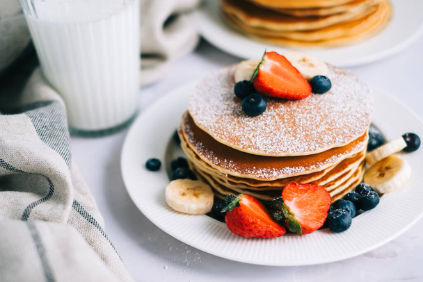 Tasty pancakes with strawberry, blueberry and banana in a white plate on the table. - Photo, image