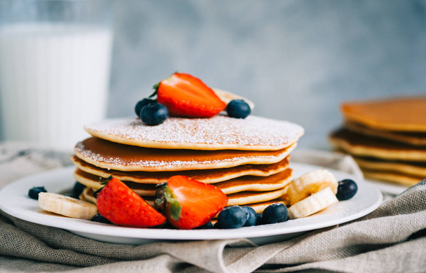 Tasty pancakes with strawberry, blueberry and banana in a white plate on the table. - Photo, image