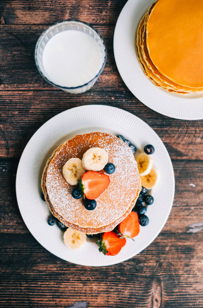 Tasty pancakes with strawberry, blueberry and banana in a white plate on the table. - Foto, afbeelding