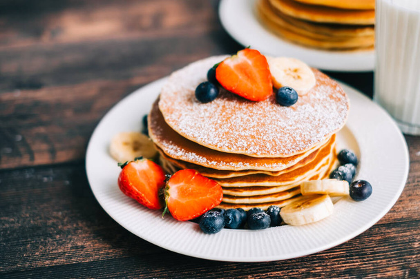 Tasty pancakes with strawberry, blueberry and banana in a white plate on the table. - Photo, Image