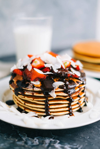 Tasty pancakes with strawberry, coconut chips and hot chocolate in a white plate on the table. - Photo, Image