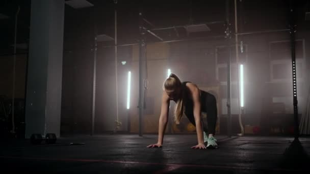Женщина делает упражнения на растяжку в темной тренажерном зале после тренировки, фитнес-женщина работает над основными мышцами в темном тренажерном зале - Кадры, видео
