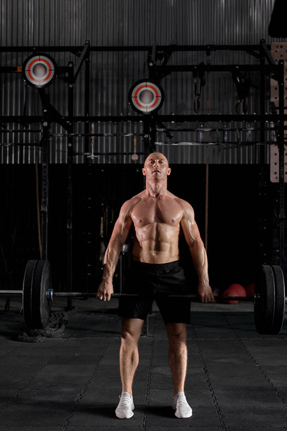 Ajuste atleta hombre sano haciendo ejercicio con pesadas barras en el moderno gimnasio oscuro. - Foto, Imagen