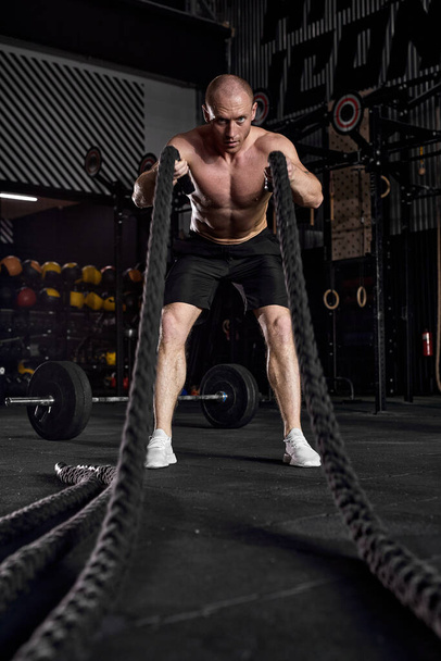 Sport. Battle ropes session. Attractive young fit sportsman working out - Fotó, kép