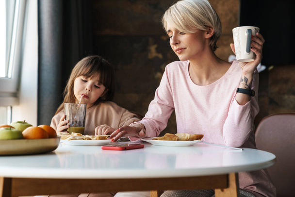 Blonde young mother and her little daughter having breakfast - Foto, Imagem