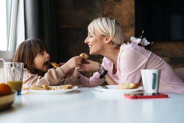 Happy young mother and her little daughter having breakfast - Foto, afbeelding