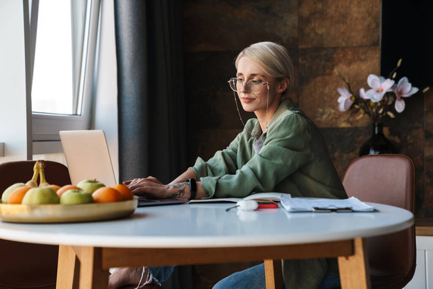 Orta yaşlı, kısa saçlı bir kadın. Evde otururken bilgisayarla video çalışıyor ya da çalışıyor. - Fotoğraf, Görsel