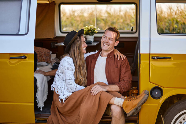 Beautiful cheerful couple sitting inside of campervan while looking outside of the van - Foto, Imagen