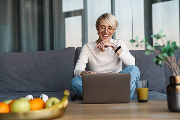 Smiling mid aged blonde woman studying online via laptop computer in the living room - Photo, Image