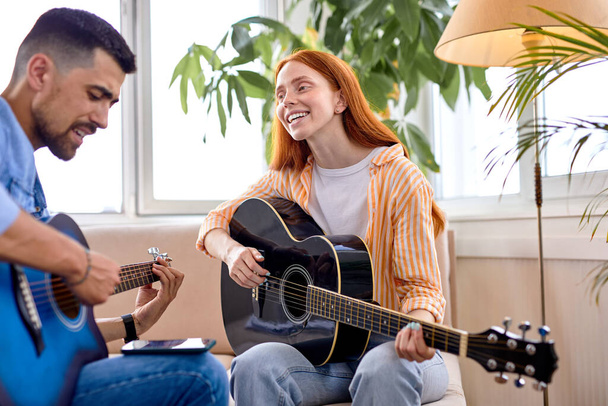 Bearded stylish man and beautiful woman playing song on guitar instrument - 写真・画像