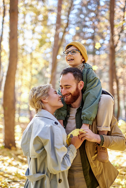 friendly couple with son hugging kissing and having fun in autumn park or forest - Фото, изображение
