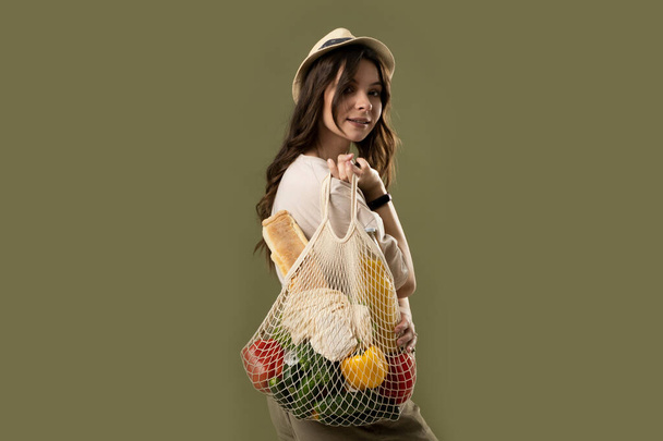 Zero waste concept. Young beautifull brunette woman holding reusable mesh shopping bags with vegetables, products. Eco friendly mesh shopper. Zero waste, plastic free concept. - Photo, image