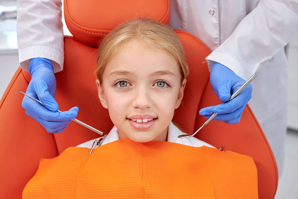 Kid girl came to see the dentist. Kid sits in dental chair. Cropped dentist bent over her - Фото, изображение