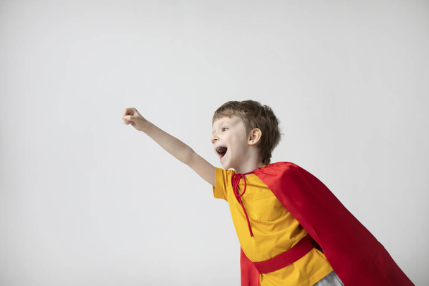 Cheerful child is playing in superhero in red cloak, holding out his hand. Superpowers boy want to fly. - Foto, immagini