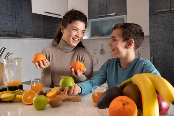 Beautiful happy mother preparing juice from fresh fruit in the kitchen with her son - Photo, Image