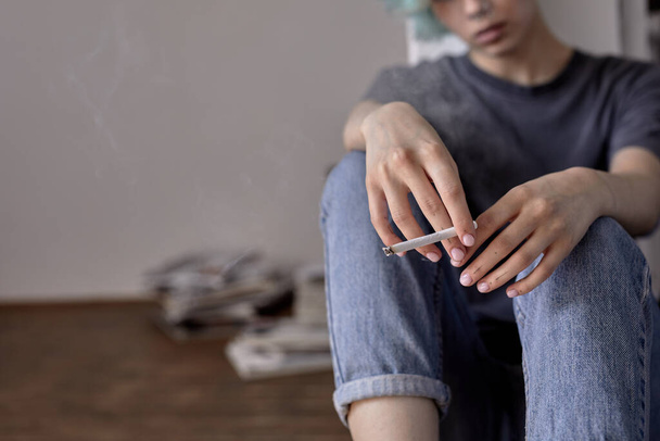 Cropped close-up woman hands holding cigarette in hands while sitting on floor alone - Foto, afbeelding