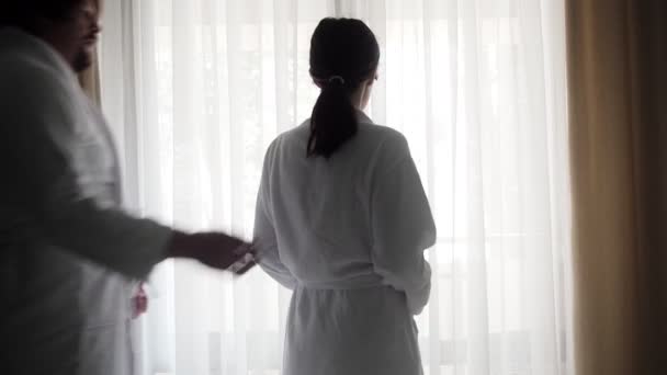 Scene in the hotel. Couple in the morning at the window in the hotel room. The husband approaches and hugs the woman. Couple enjoying a moment together on vacation - Footage, Video