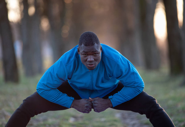 Black sportsman stretching legs after workout in nature in winter time - Foto, Imagen