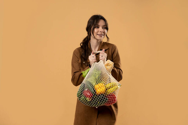 Zero waste, plastic free concept. Young brunette woman with cotton reusable mesh bag with fruits and vegatables. Shopping without plastic packaging in plastic free grocery store. - Foto, Imagen